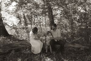 A black and white photo captures a family moment on a rustic log in the woods.
