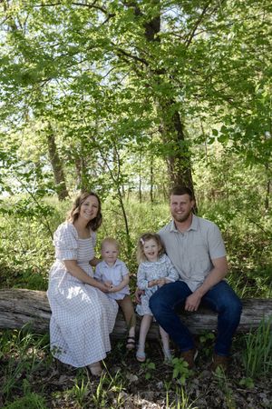 A family sits together on a fallen tree trunk surrounded by green foliage.