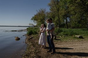 A family walks along a scenic lakeside shore on a bright sunny day.