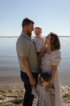 A joyful family embraces on a sunny beach with calm waters in the background.