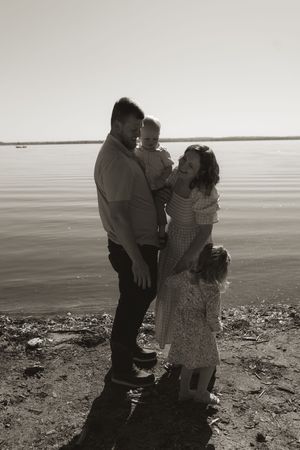 A family shares an intimate moment together on a rocky beach shoreline at sunset.