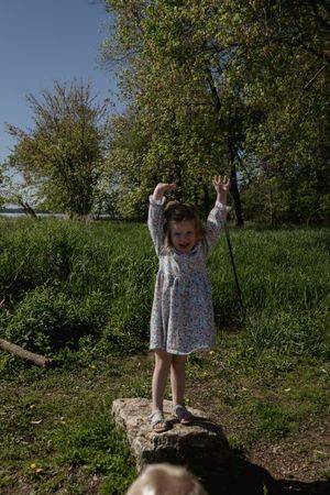 A child stands playfully on a rock in a green spring landscape.