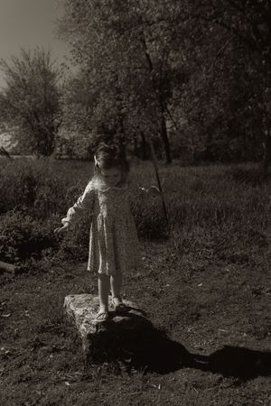 A black and white image of a child standing on a rock in nature.