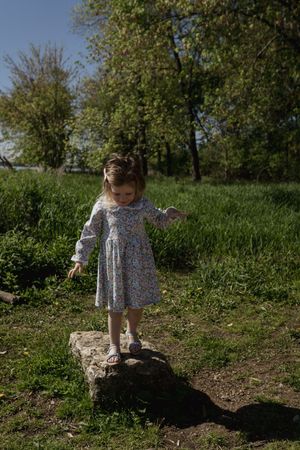 A small child explores a grassy hillside path on a sunny afternoon.