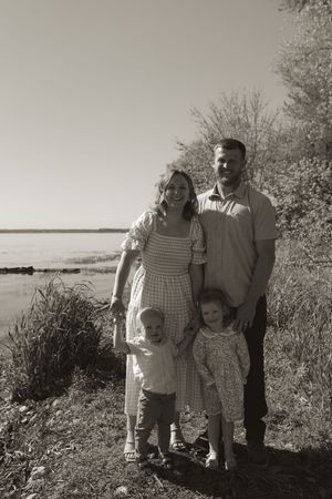 Family enjoying a sunny day by the waterfront with greenery and trees in the background.