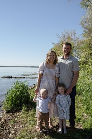 Family posing together on a grassy hill overlooking a scenic lake on a bright summer day.