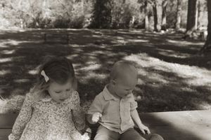 Black and white photo of children sitting together on a bench in a park setting.