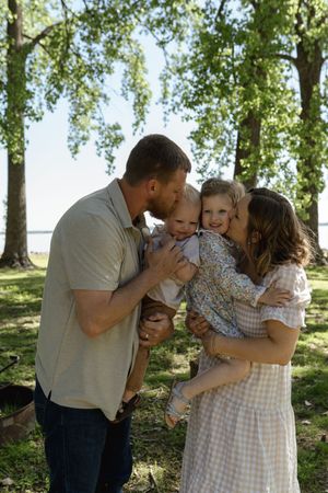 Family sharing an intimate moment together under green trees in a park.