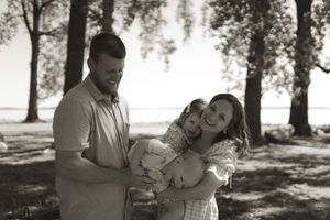 Black and white portrait of a family embracing outdoors with trees in background.