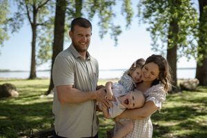 Family portrait session captured in natural sunlight under tall trees by a lake.