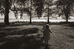 Scenic landscape photo of figures walking under trees with water in the background.