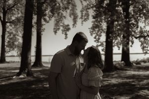 A couple shares an intimate moment in a sun-dappled park setting with trees in the background.