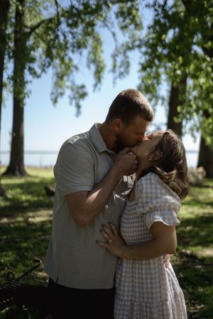 A tender moment between a couple in casual attire against a backdrop of leafy trees.