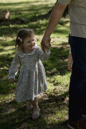 A small child in a floral dress plays in the dappled sunlight beneath tall trees.