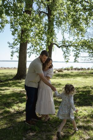A family enjoys a playful moment together on a grassy hill under tall trees.