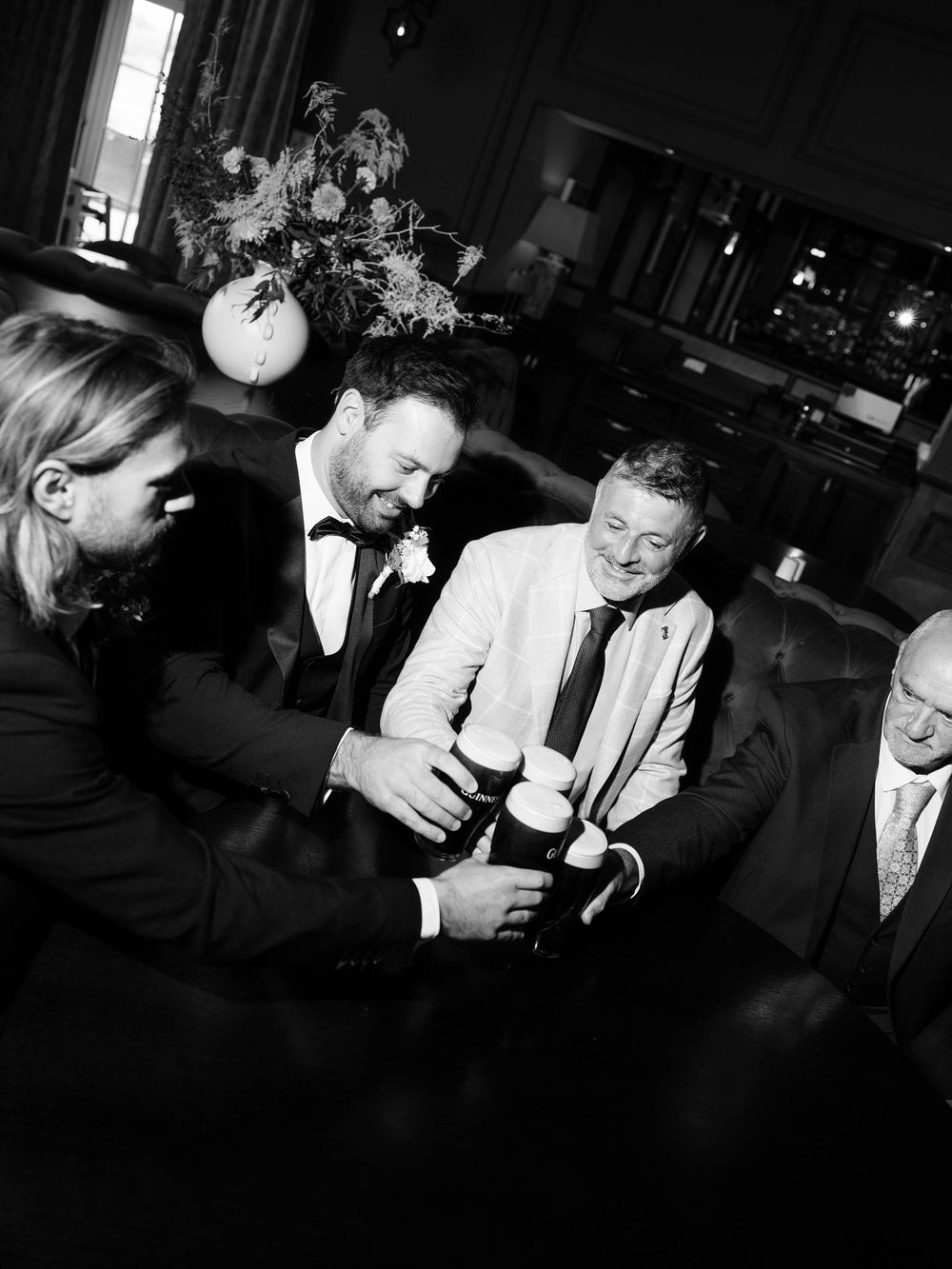 A black and white photo of men in tuxedos and formal attire gathered at what appears to be an evening event.