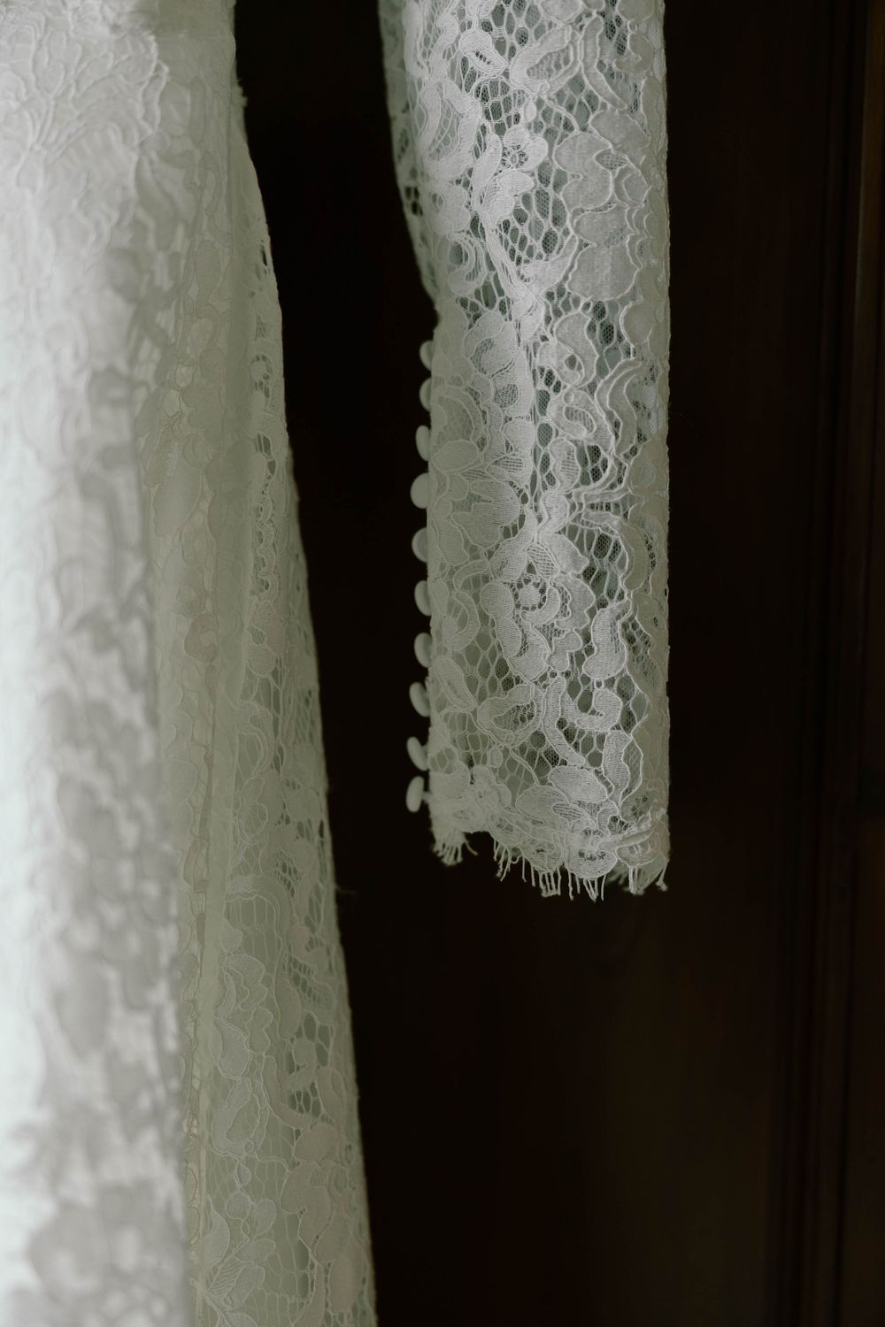 Close-up view of delicate white lace wedding dress trim against a dark background.