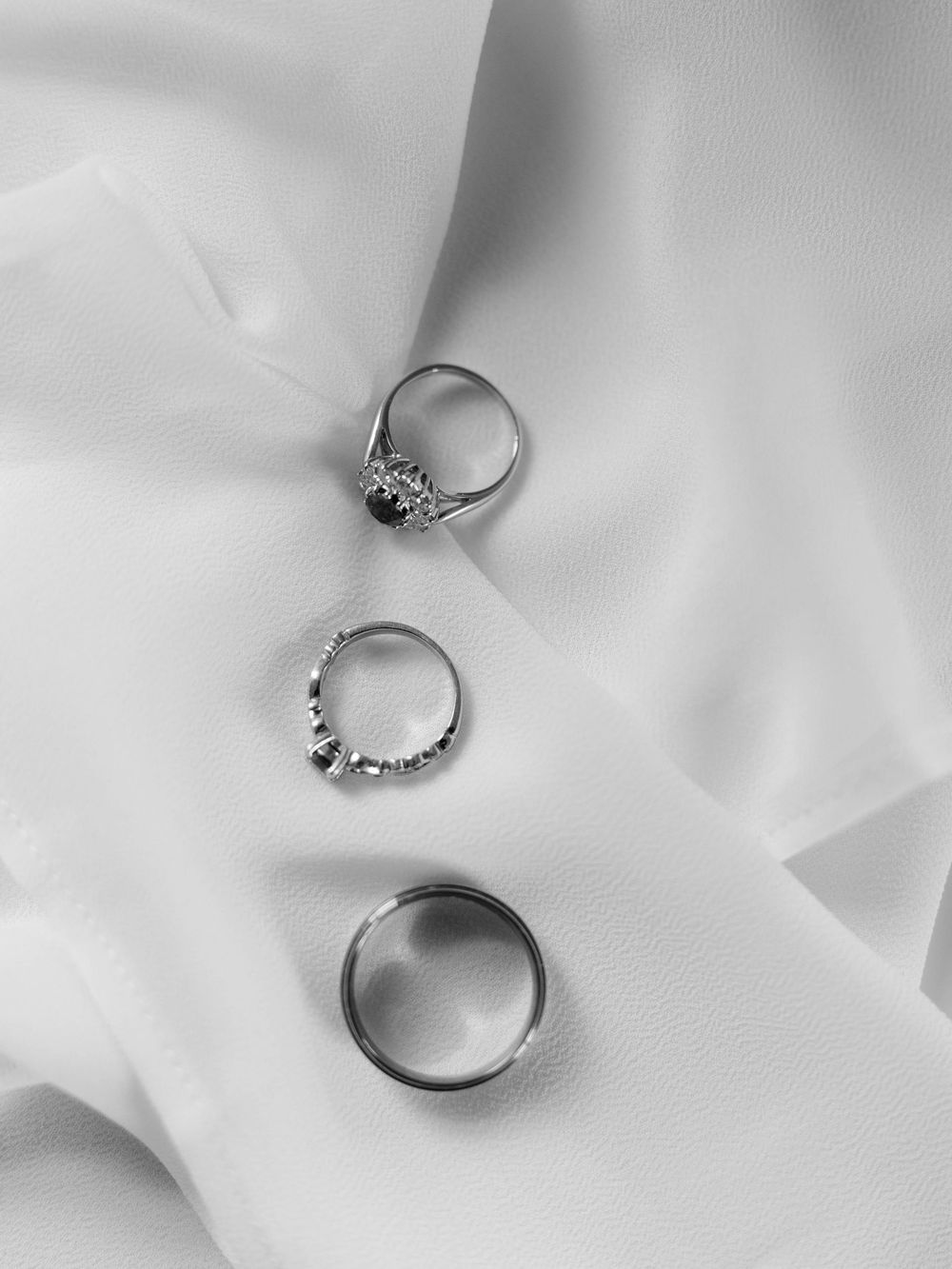 Three silver wedding rings arranged vertically on white silk fabric in black and white.