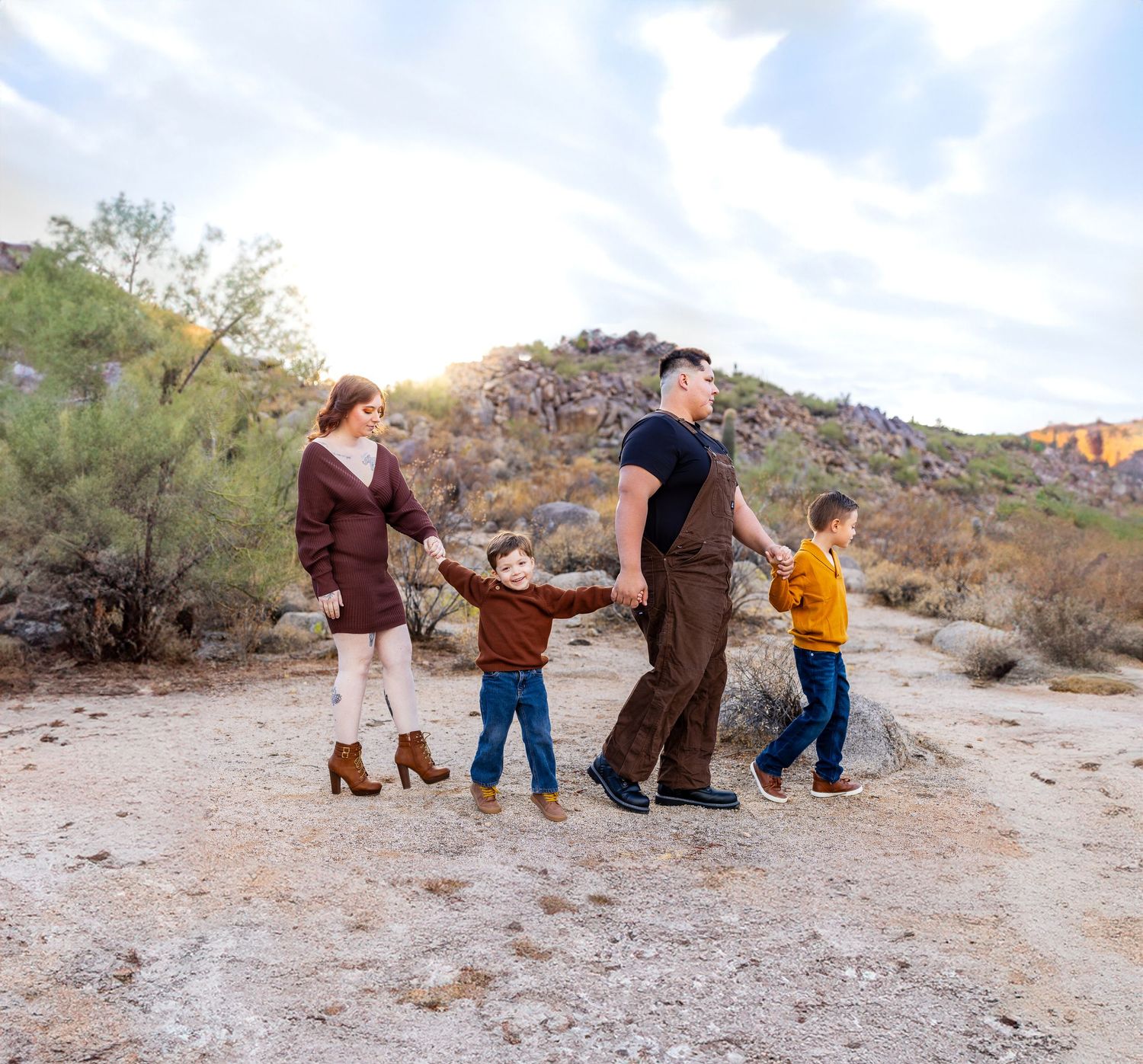 A family enjoys a walk together on a desert trail with mountains and blue sky in the background.