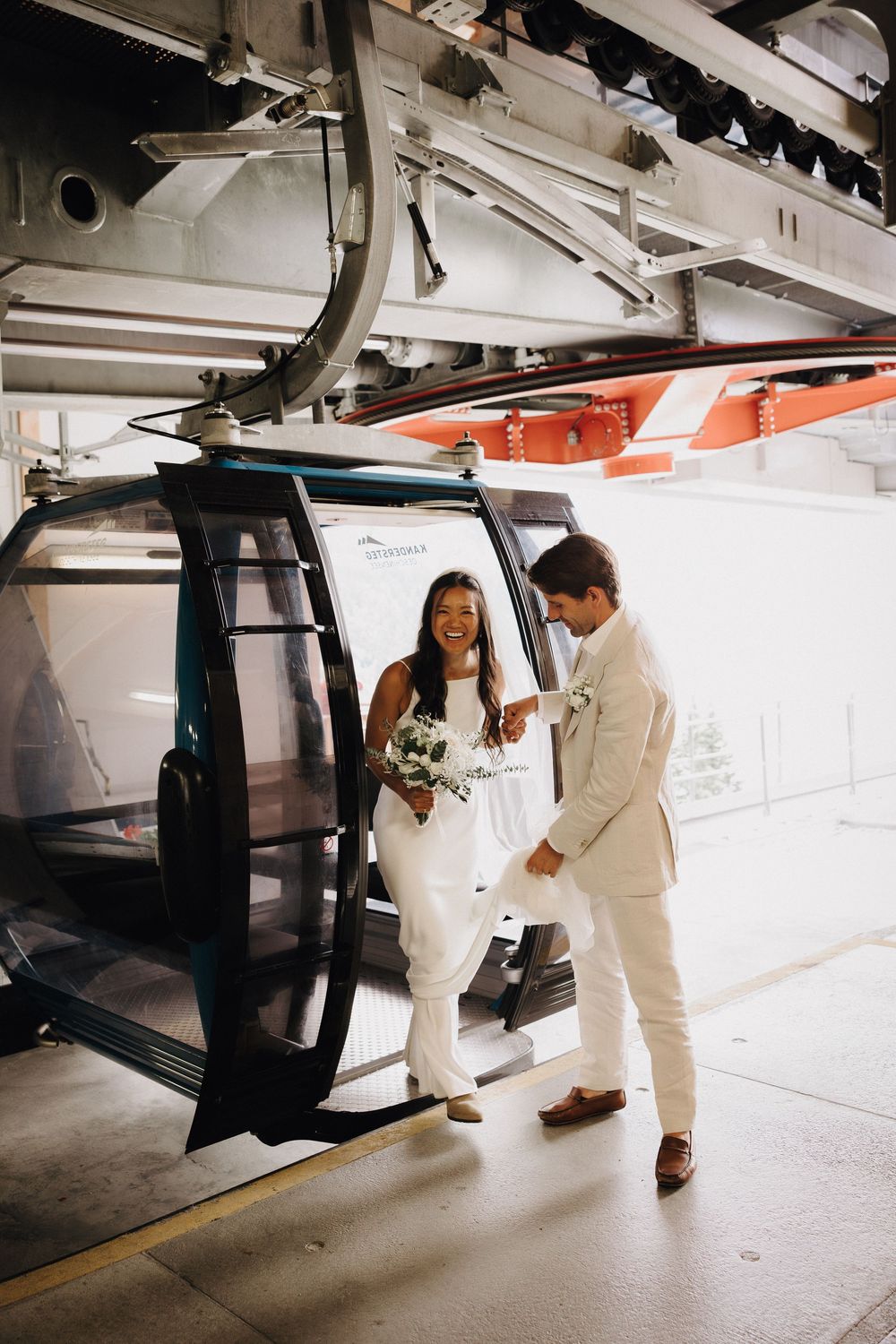 A couple dressed in white wedding attire enters a sleek modern gondola lift station.