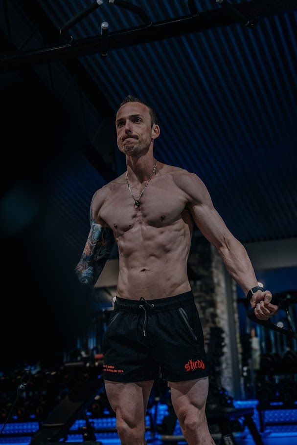 Athletic person with tattoos training shirtless in dark gym setting.