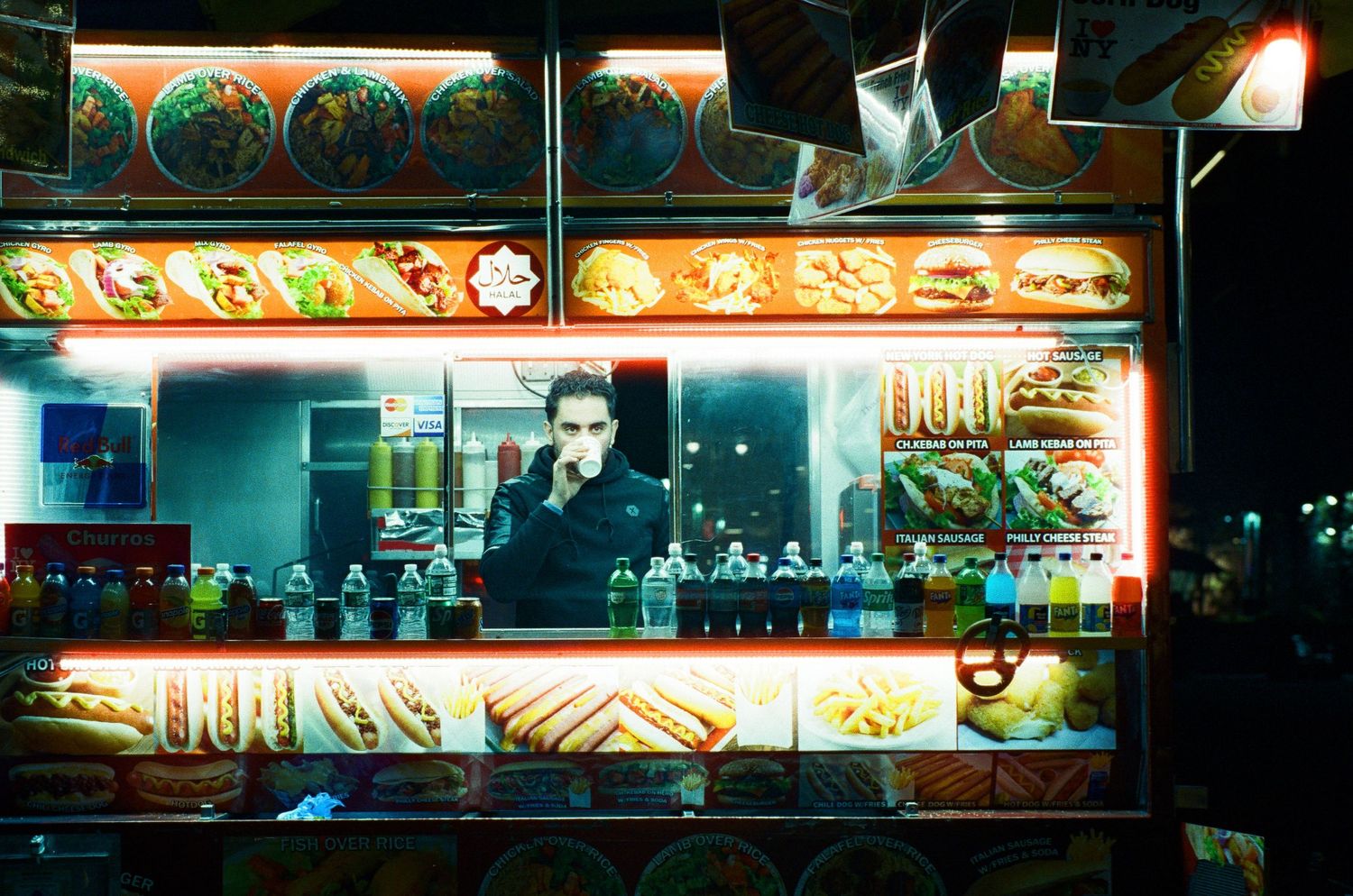 Bright neon-lit food vendor stall selling snacks at night.