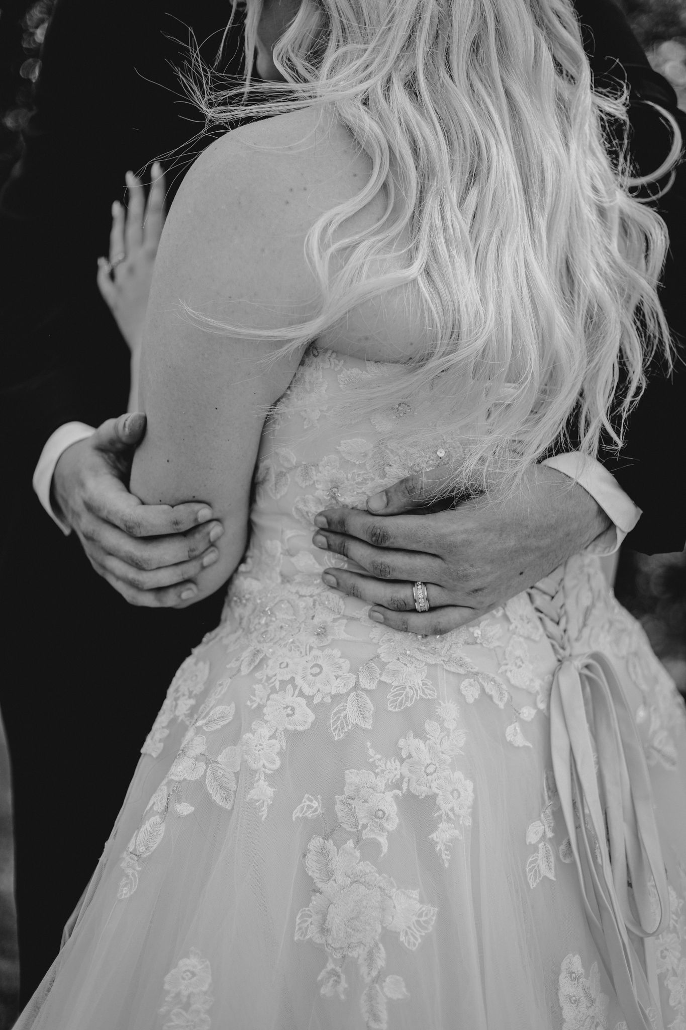 Close-up black and white photo of hands embracing a bride in a lace wedding dress.