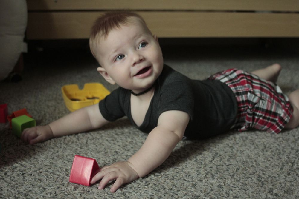 Image of a baby laying on it's belly, pushing up with his arms and smiling at someone off camera.