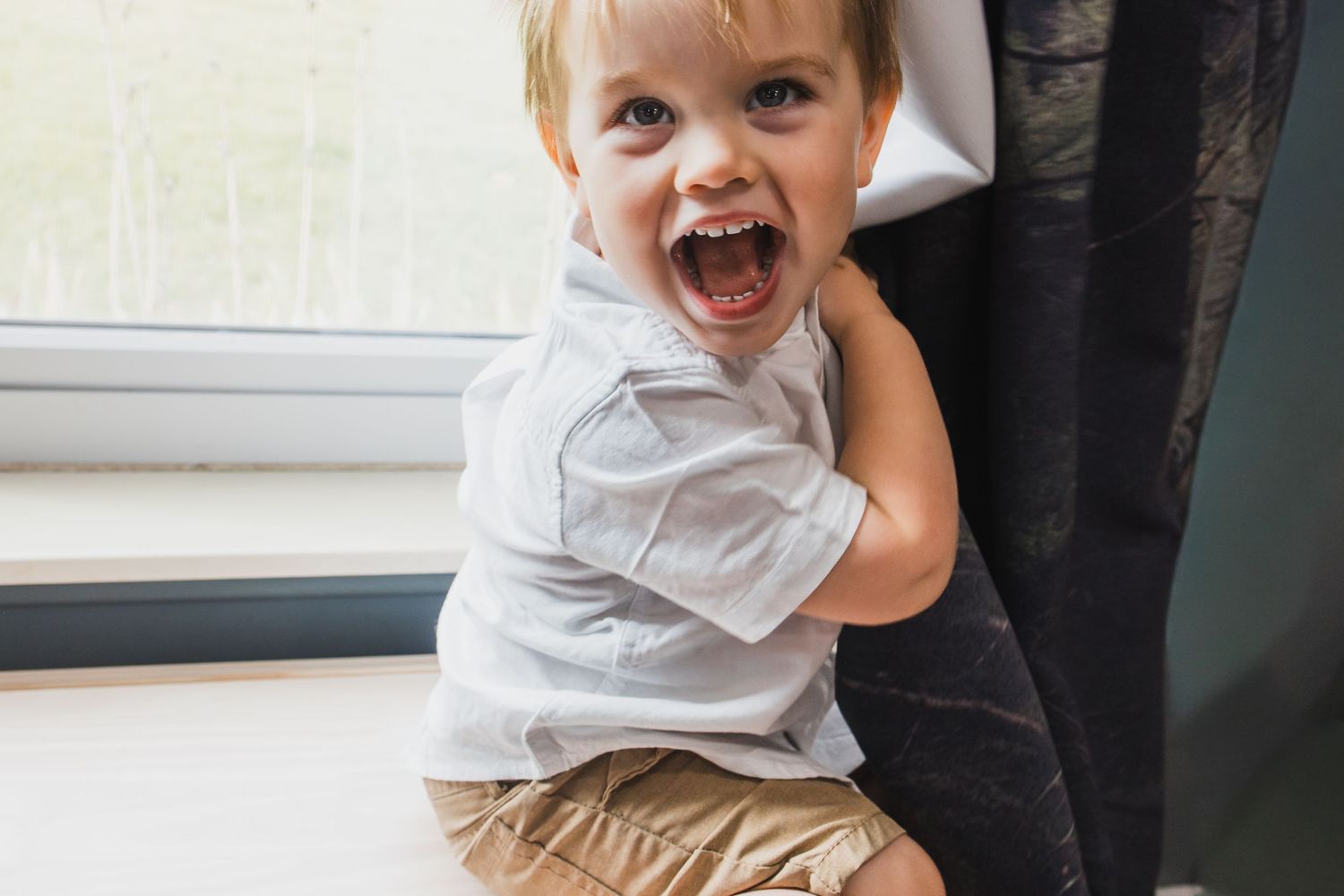 Child laughing and playing indoors in casual clothing.