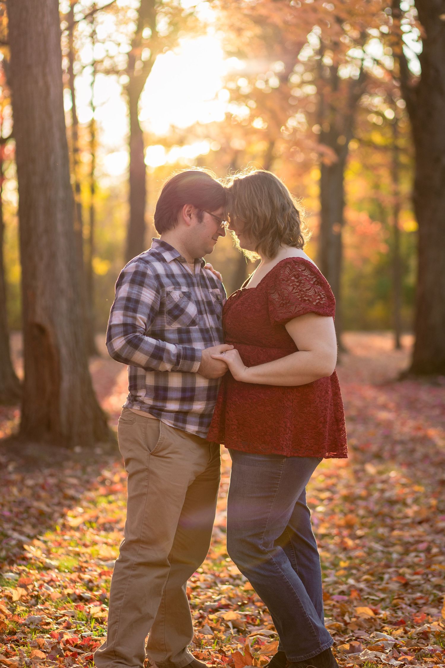 Couple dancing together among fallen leaves in autumn forest at sunset.