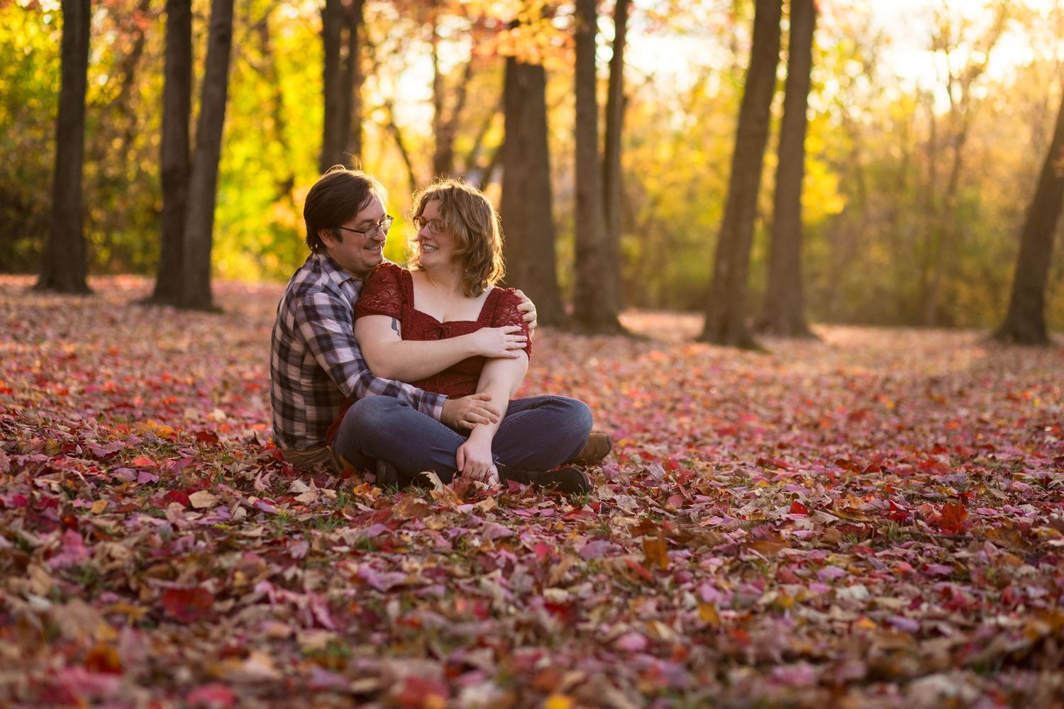 Two people share a romantic moment among fallen leaves in an autumn forest at golden hour.