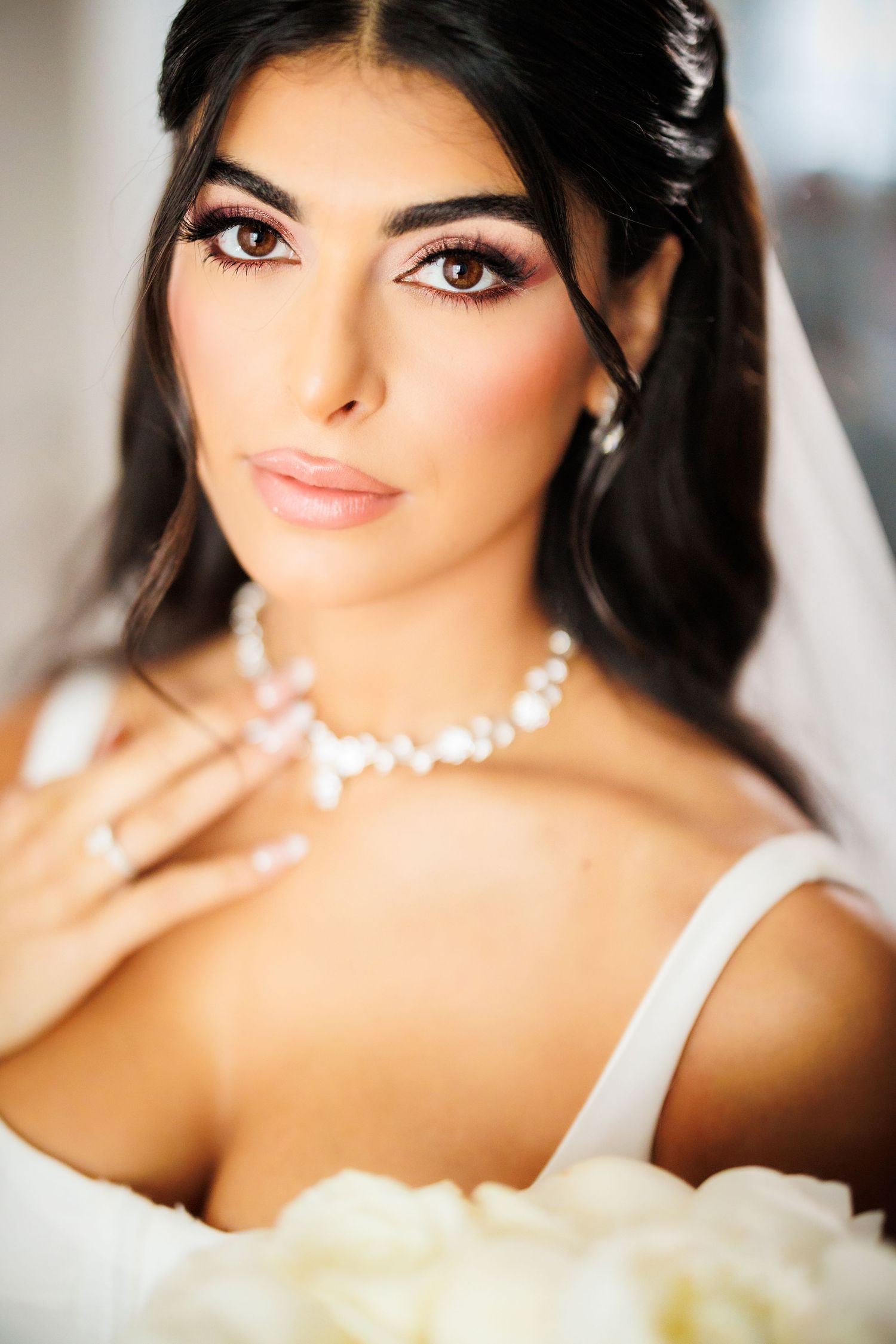 Portrait of a bride wearing white with pearl necklace and glamorous wedding makeup in soft natural lighting.