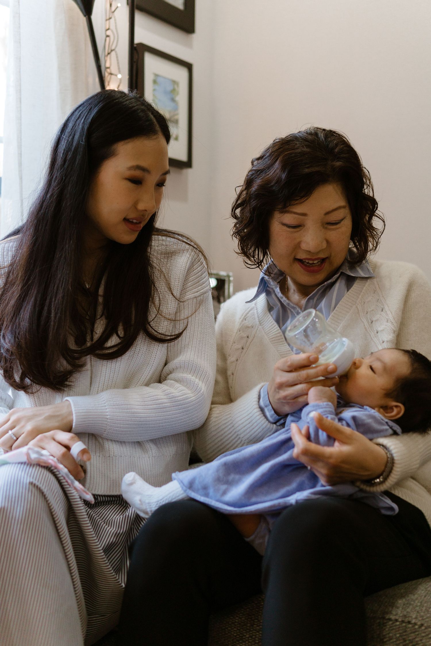 Three generations sharing a tender family moment on a couch as they feed and care for a baby together.