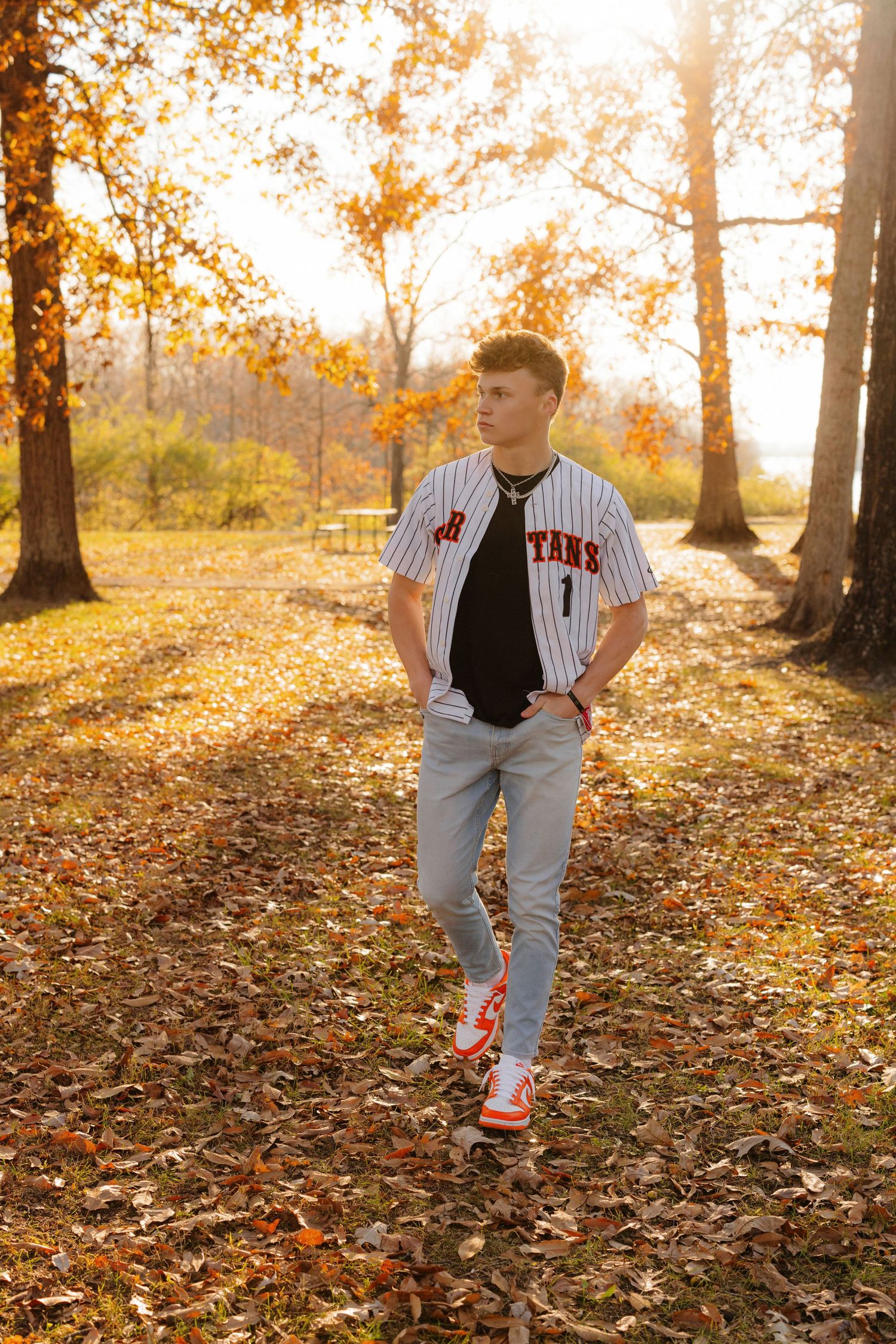 Person in Yankees jersey walks on autumn path covered in fallen leaves during golden sunset lighting.