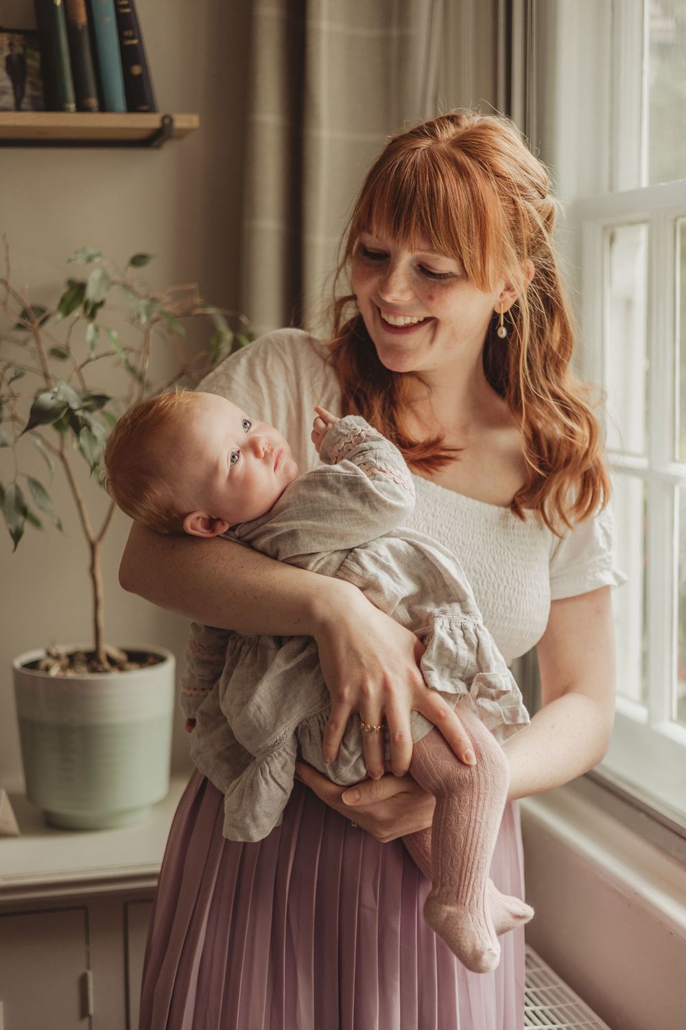 mum holding baby in a lounge, by a large window