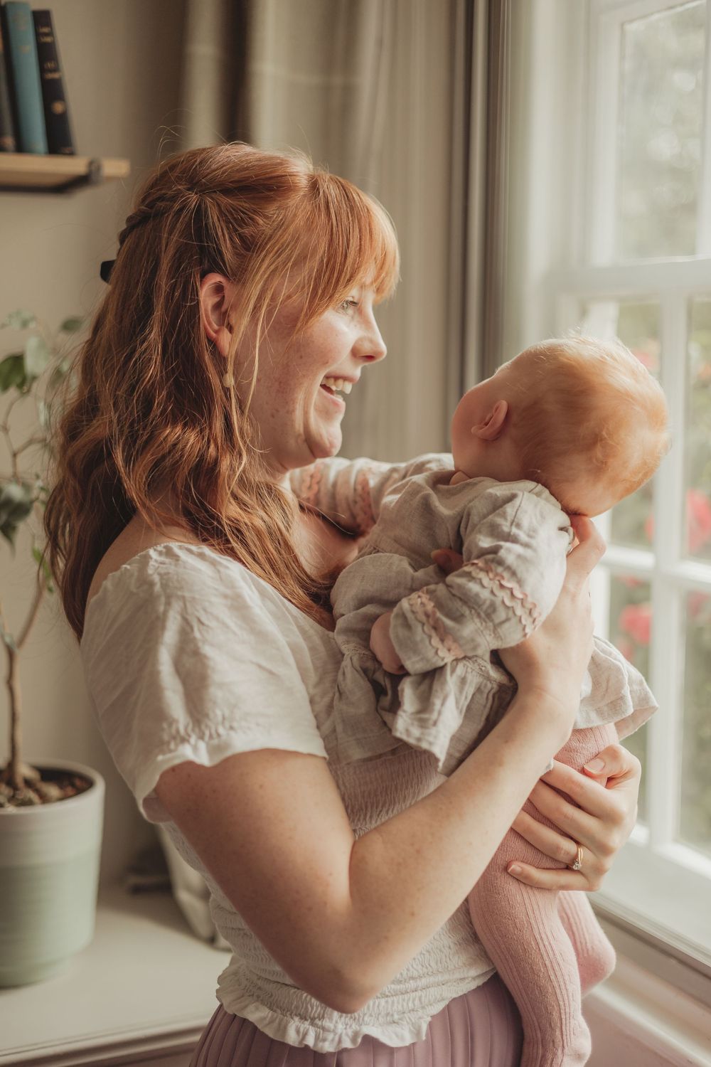 mum holding baby in a lounge, by a large window