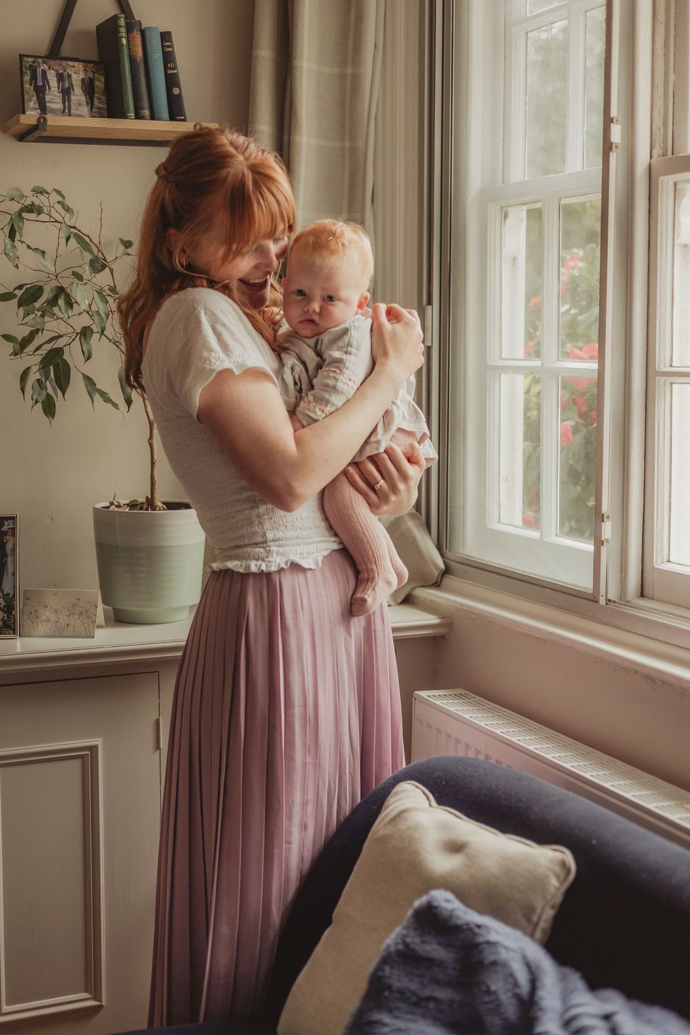mum holding baby in a lounge, by a large window