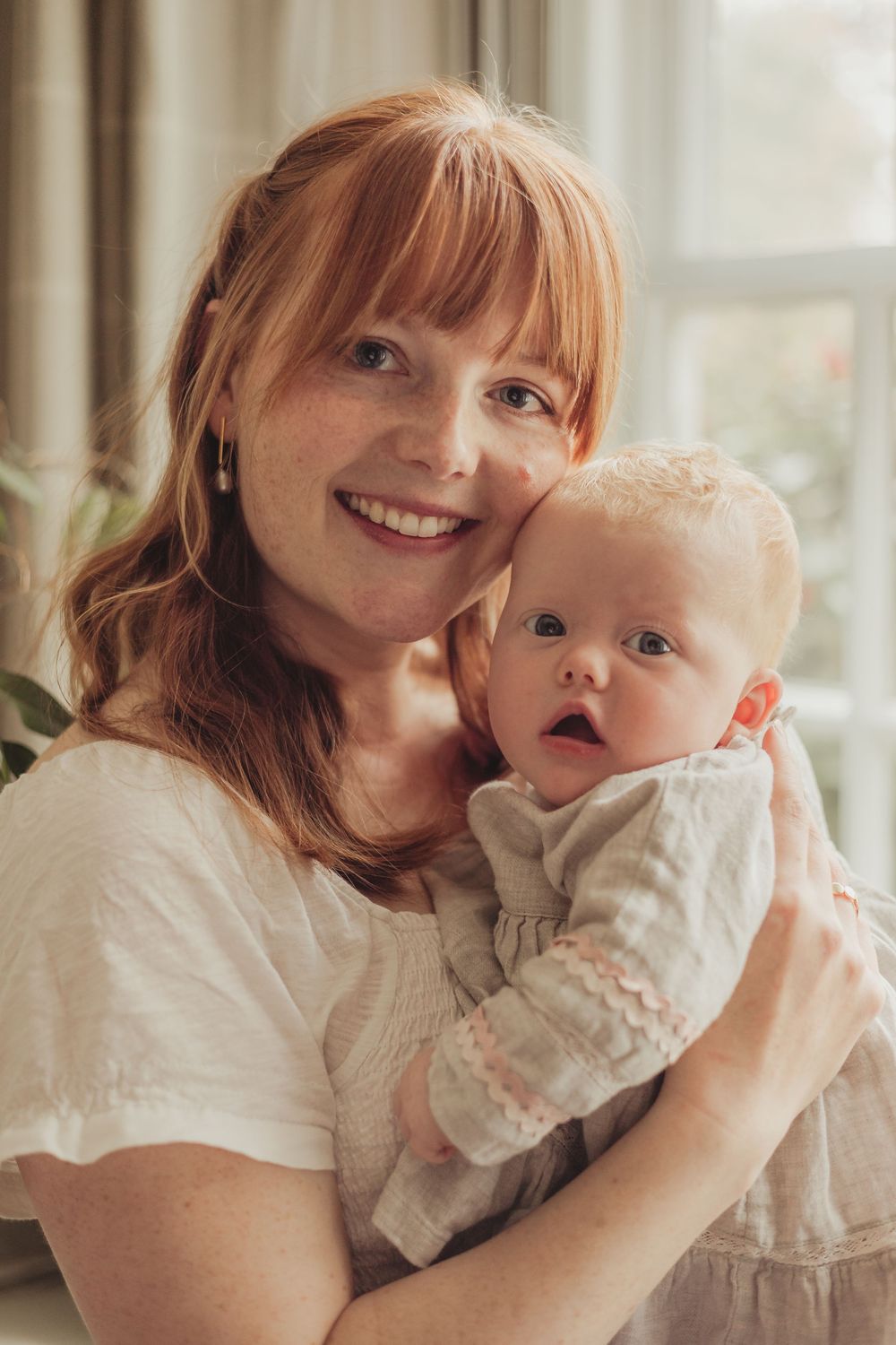 mum holding baby in a lounge, by a large window