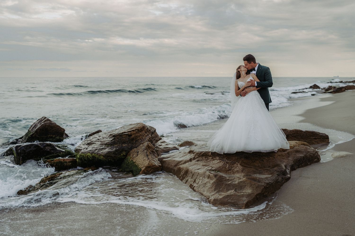 Romantic beach wedding photo of couple lying on sand at sunset.