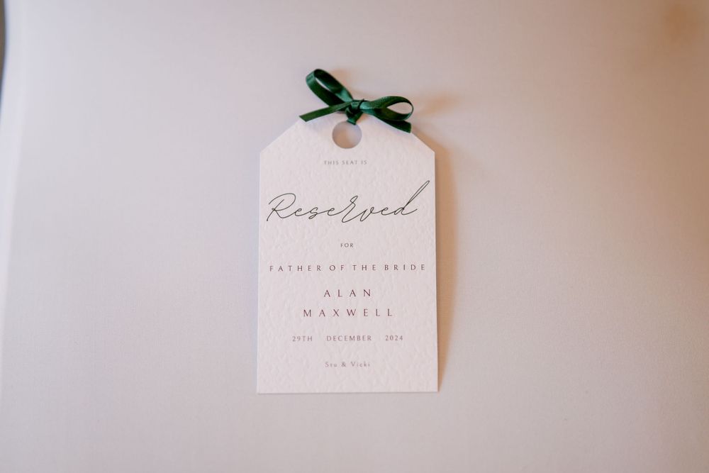 An elegant white wedding RSVP tag with a green ribbon bow attached at the top.
