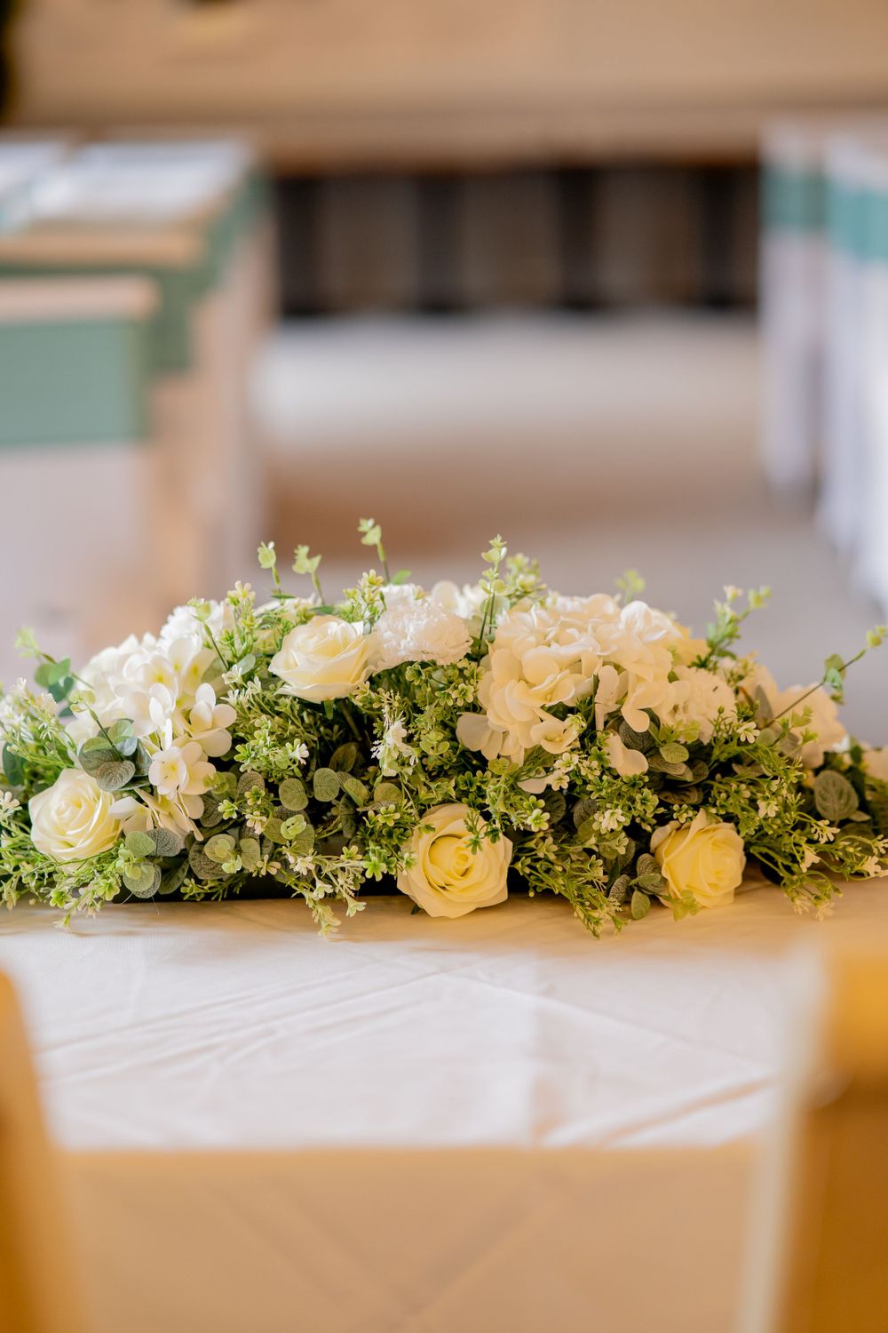 Elegant floral centerpiece with white roses and delicate greenery arranged on white tablecloth.
