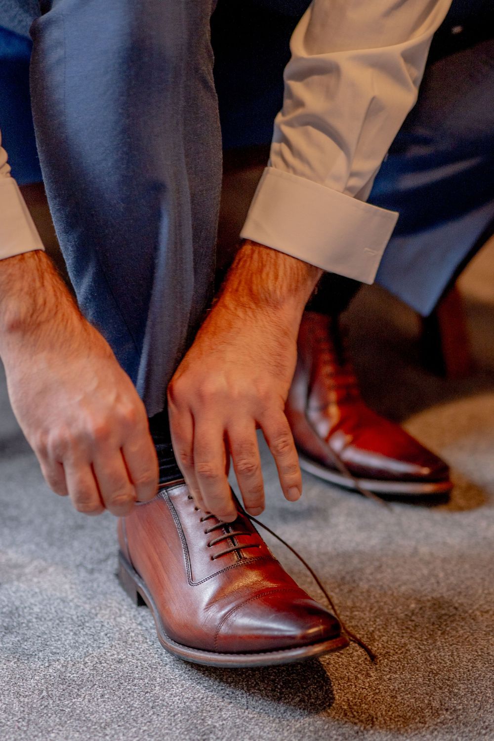 Close-up of hands tying laces on polished brown leather dress shoes.