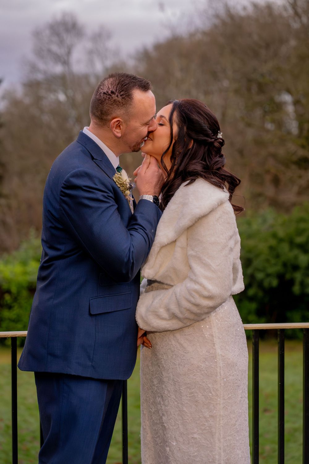 A romantic winter wedding moment captured outdoors showing a couple sharing a kiss in formal attire.