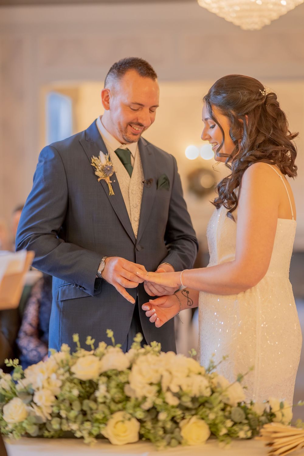 A tender moment during a wedding ceremony as a couple exchanges rings in front of elegant white floral arrangements.