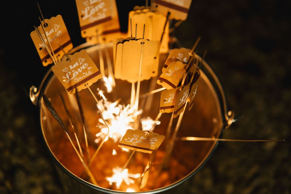 Sparklers illuminate decorative signs in a metallic bucket creating a festive wedding display.