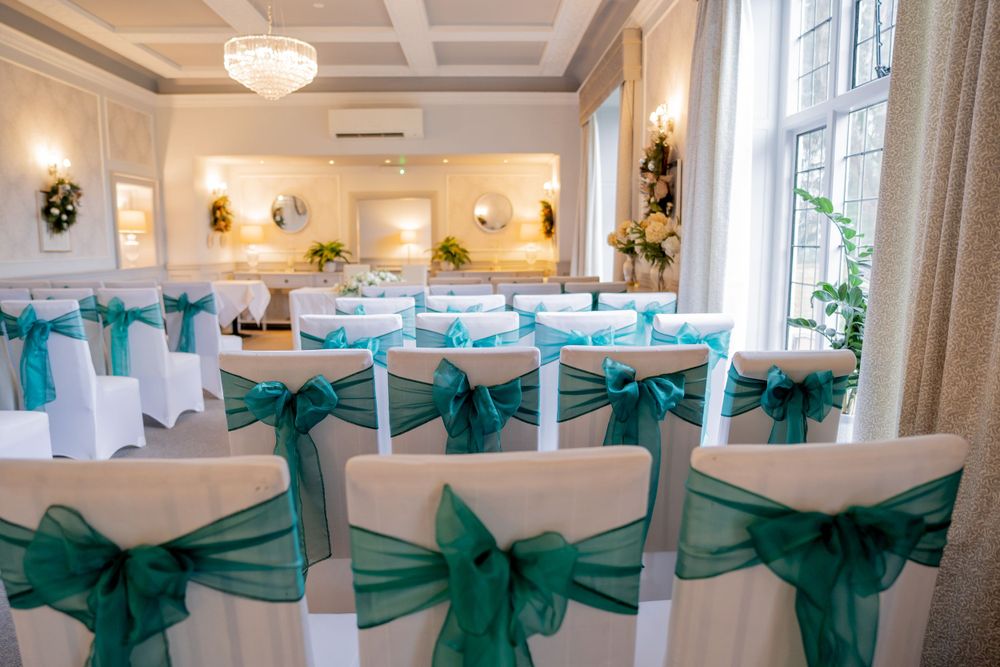 Wedding ceremony venue with white chairs decorated with teal sashes and elegant chandelier lighting.