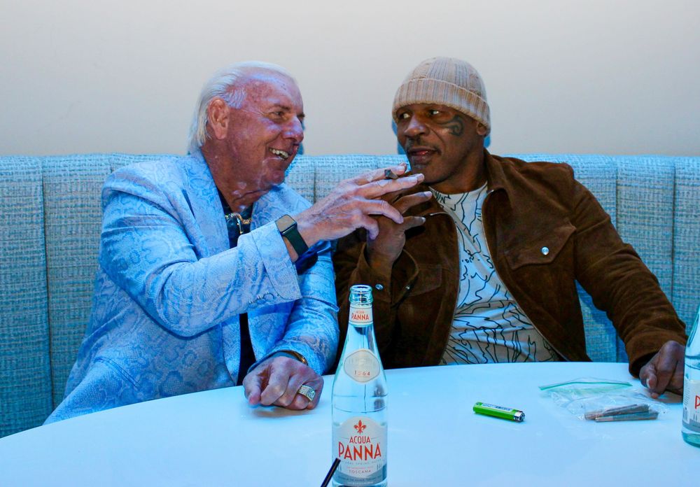 Two elderly men laughing and conversing while seated at a table with drinks.