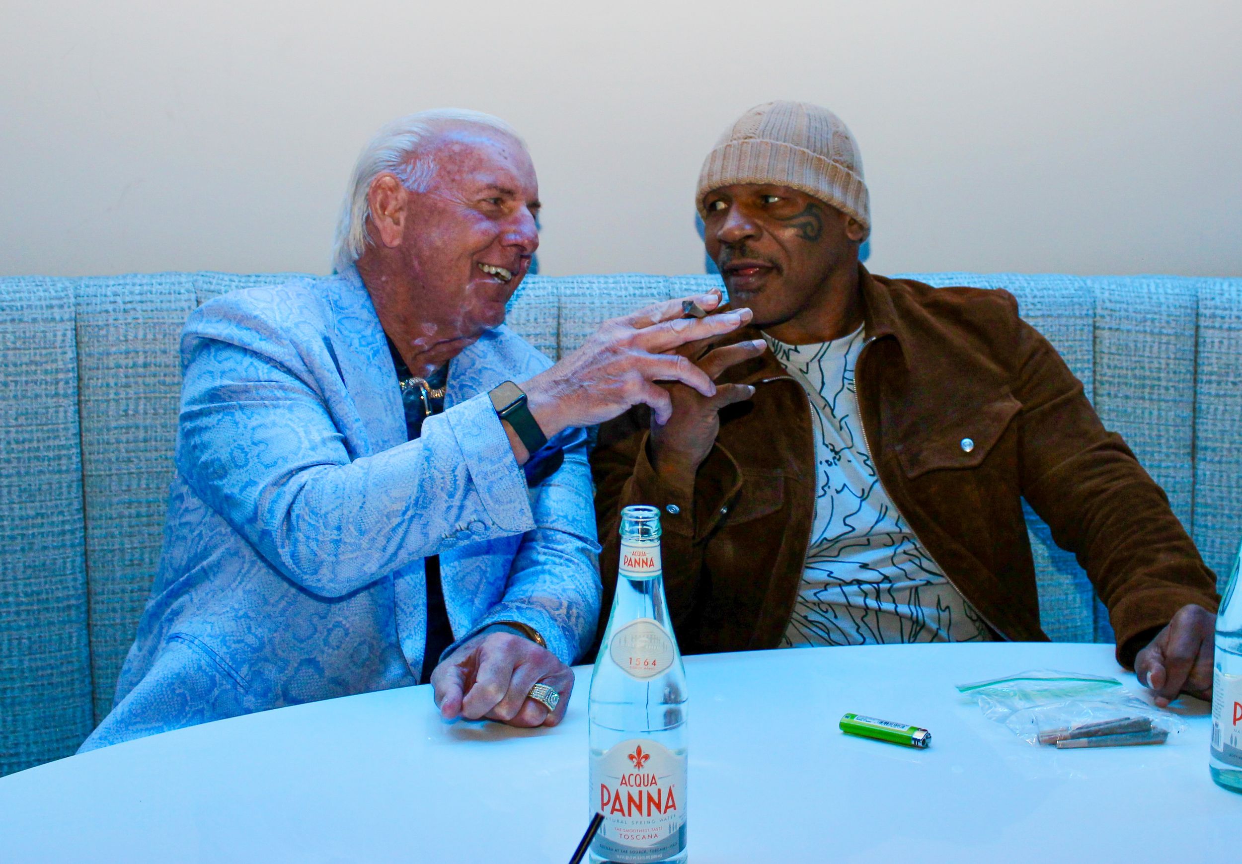 Two elderly men laughing and conversing while seated at a table with drinks.
