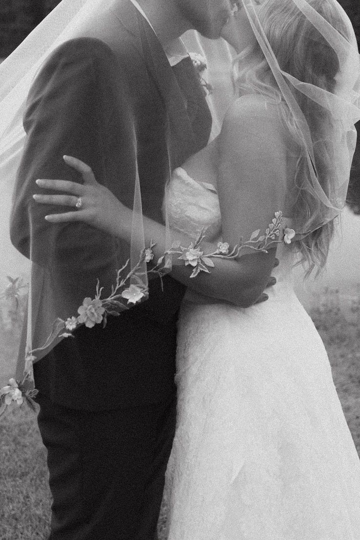 Black and white wedding photo showing intimate moment between couple with bride in delicate veil and white dress.