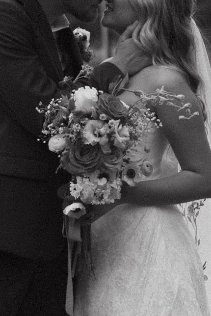 Black and white wedding photo showing a couple embracing with a beautiful floral bouquet of roses and baby's breath.